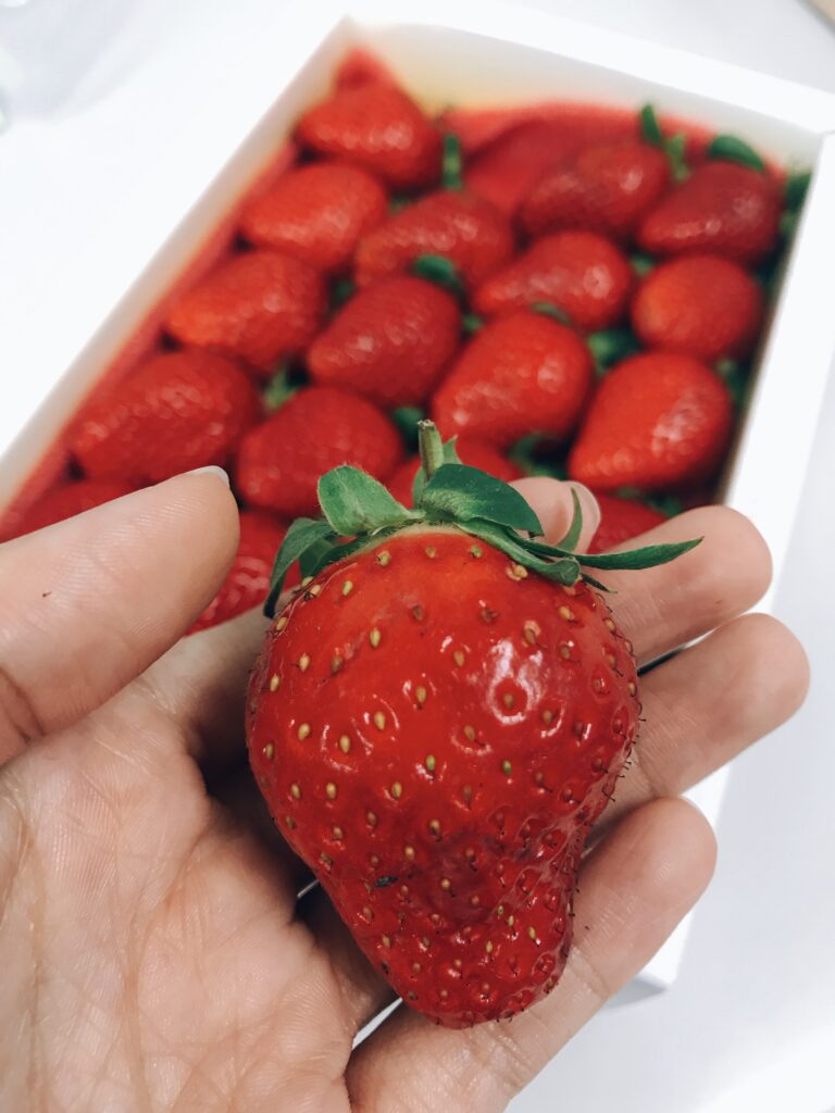 Vibrant Red Strawberry Close-Up: Freshness in Hand & Behind Wallpaper