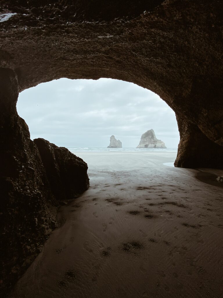 Coastal cave view with rugged rocks sandy beach sea stacks and cloudy sky serene landscape wallpaper