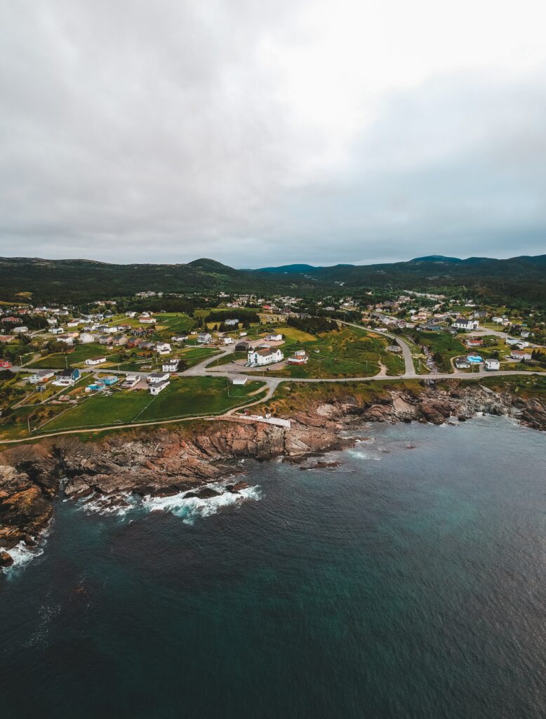 Coastal city on cliffs with charming homes green hills crashing sea under dramatic cloudy sky wallpaper