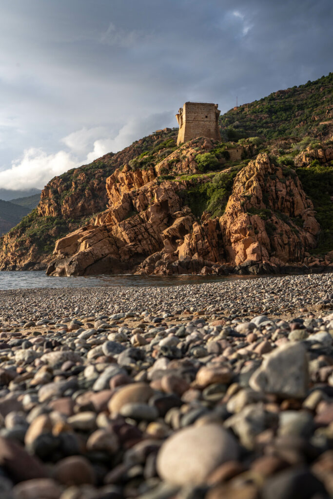 Coastal wallpaper with smooth pebbles rocky cliffs ancient stone building lush greenery and clouds
