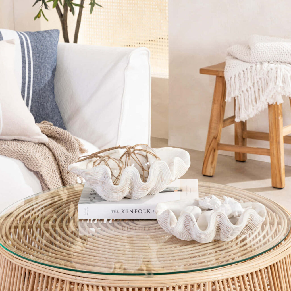 Cozy coastal interior with white clam shells on glass rattan table soft neutral tones wallpaper
