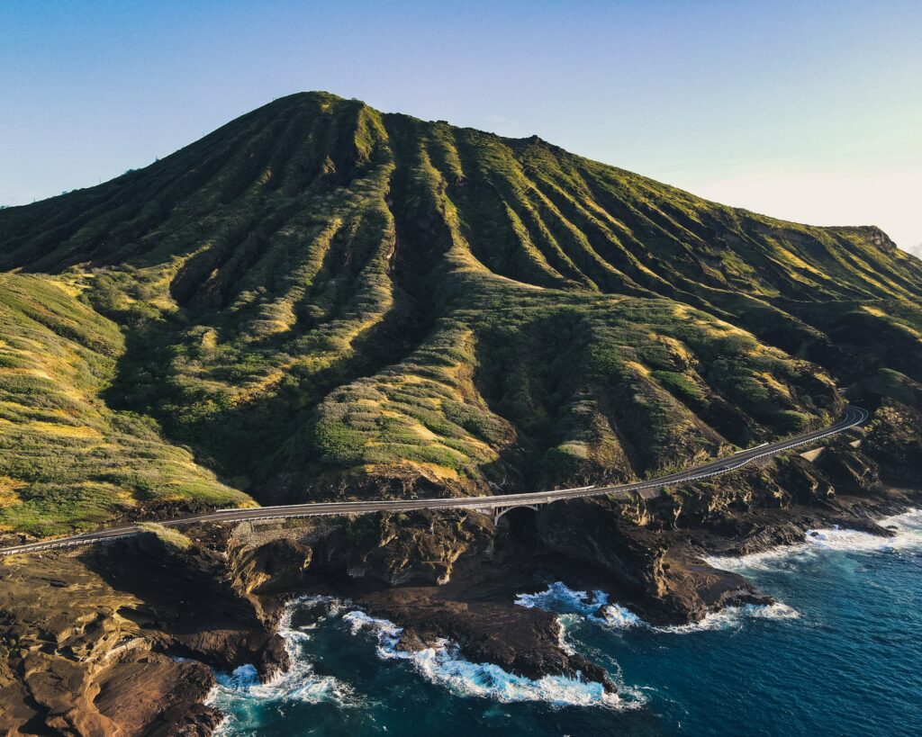 Coastal island landscape with winding cliff road lush green hills volcanic mountain sunlight Wallpaper