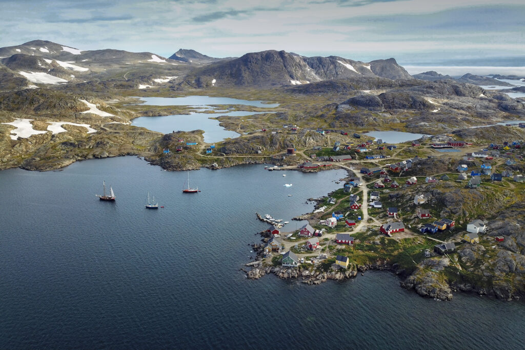 Aerial view of coastal island village with colorful buildings boats calm sea mountains snow greenery wallpaper