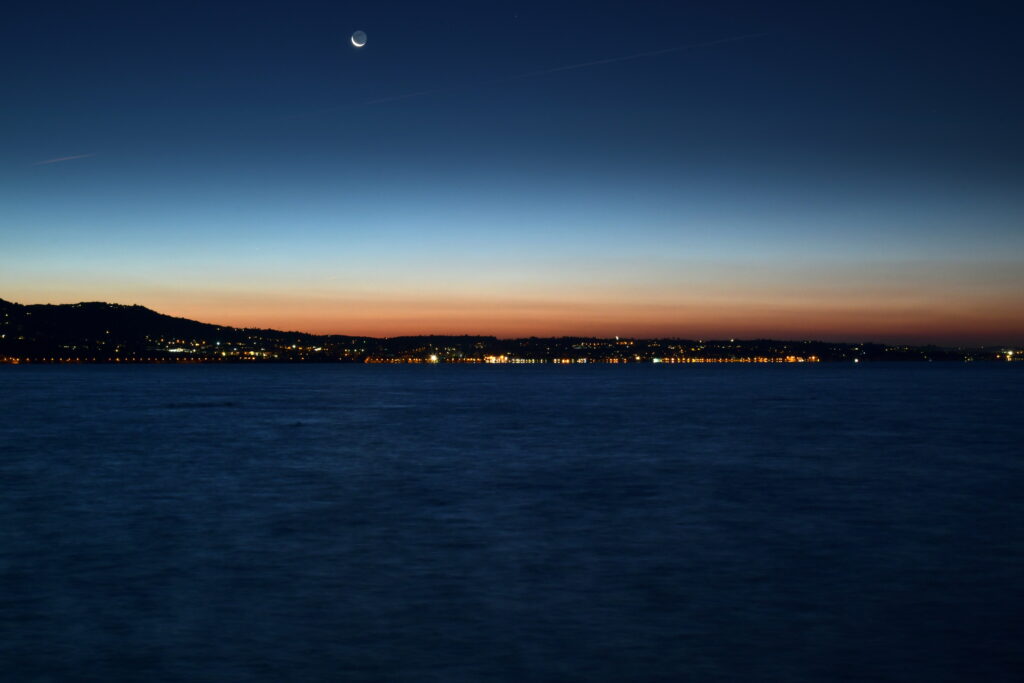 Twilight Symphony: Mesmerizing Coastal Cityscape Beneath a Horizon ablaze with Sunset Splendor Wallpaper