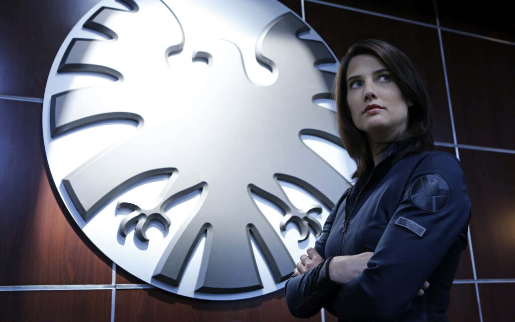 Cobie Smulders as S.H.I.E.L.D agent in dark tactical suit with high tech Marvel universe backdrop Wallpaper