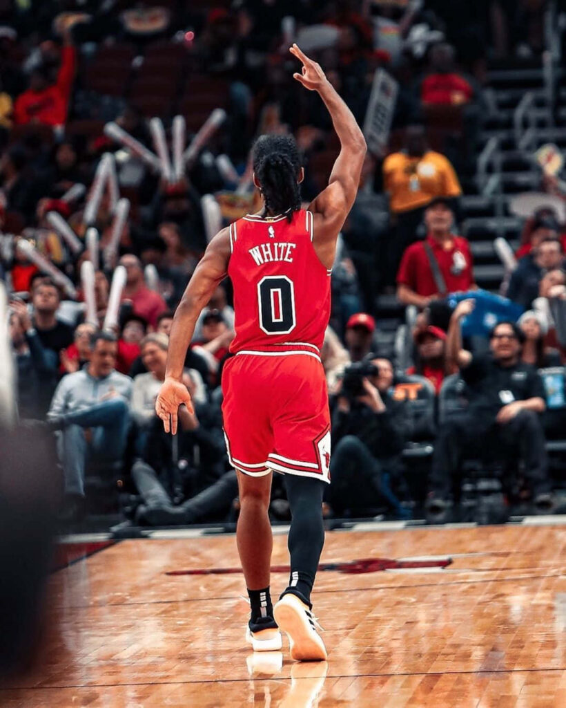 Coby White in red Chicago Bulls uniform raises arm celebrating on court with cheering fans Wallpaper