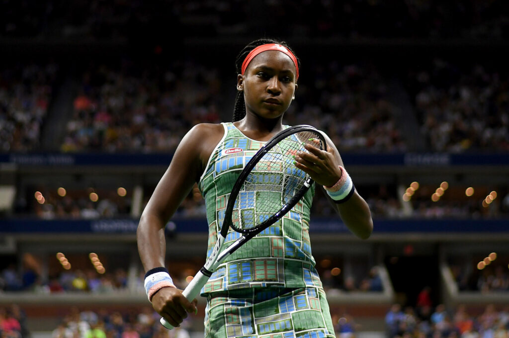 Coco Gauff in green tennis outfit on court with vibrant pattern intense stadium lights and crowd Wallpaper