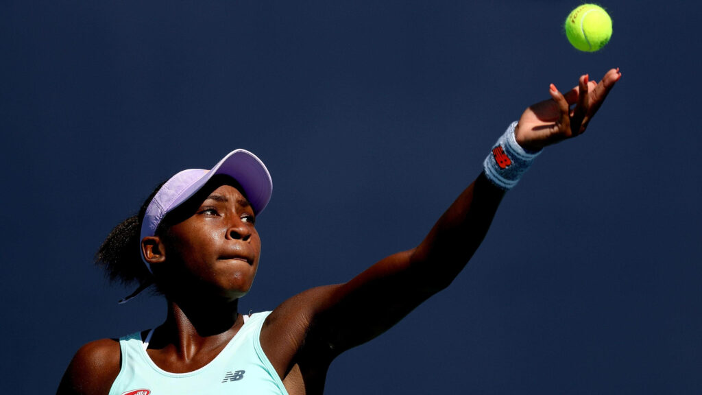 Coco Gauff mid-serve with intense focus bright yellow tennis ball against deep blue background Wallpaper