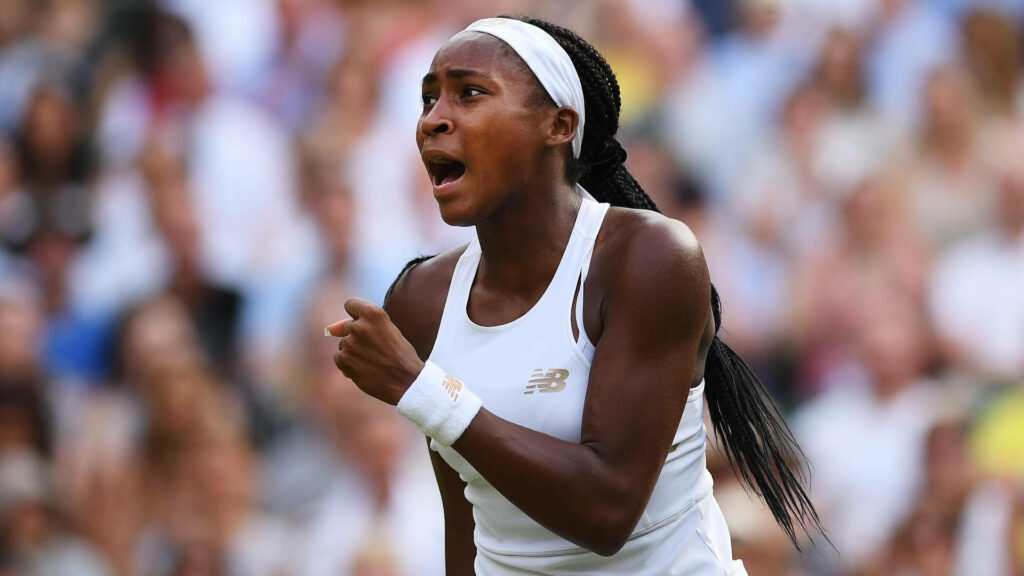 Coco Gauff in white New Balance tennis outfit focused during intense match with blurred crowd background Wallpaper
