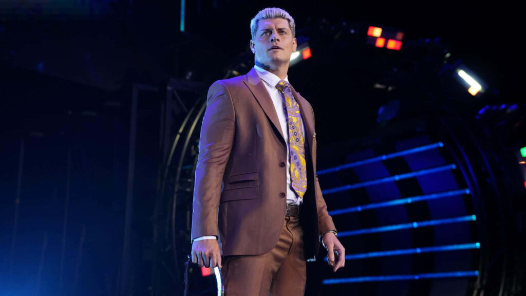 Cody Rhodes in brown suit with patterned tie on colorful stage lights high definition wallpaper