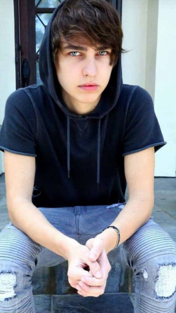 Colby Brock in black hoodie and ripped jeans sitting on stone steps with intense gaze urban style Wallpaper