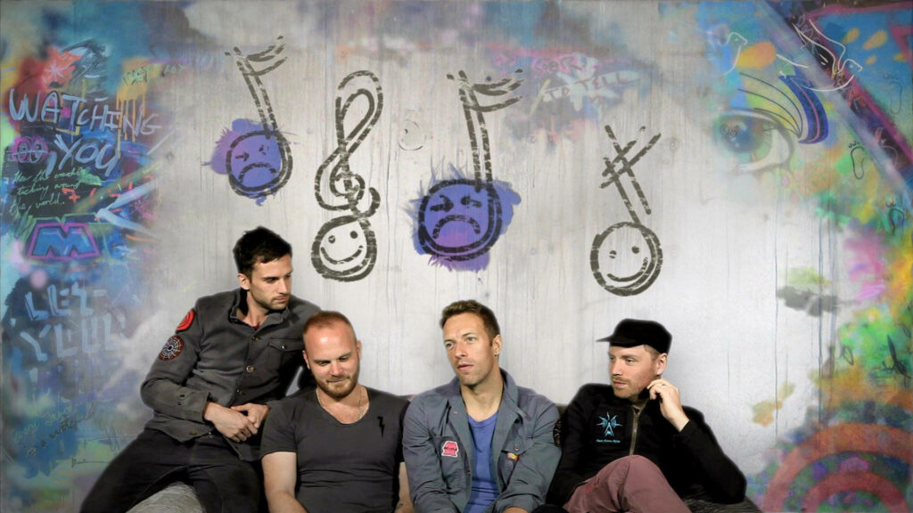 Coldplay band poses by vibrant graffiti wall with musical notes and expressive artistic faces background Wallpaper