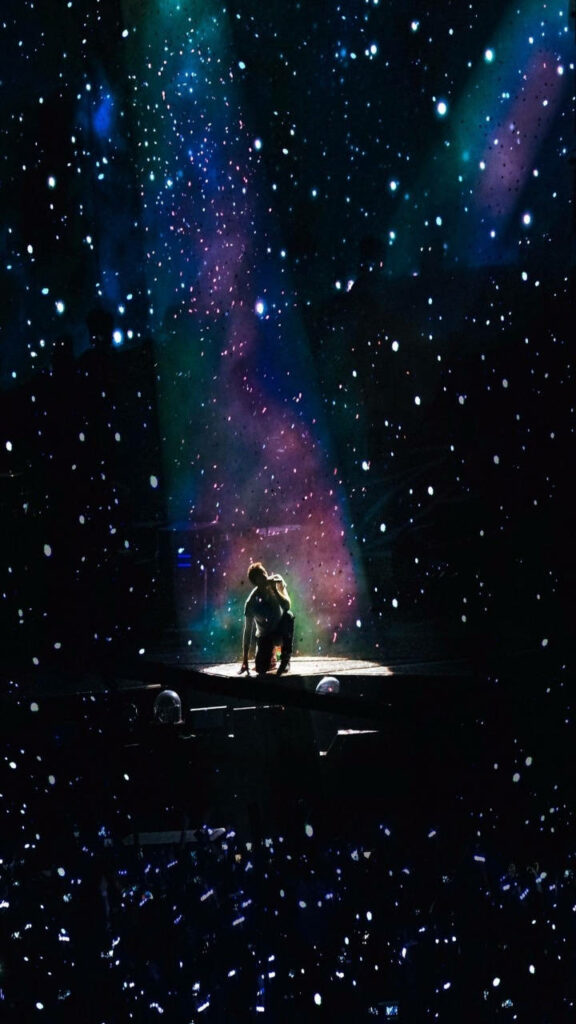 Coldplay concert wallpaper with performer under galaxy spotlight and vibrant cosmic star lights
