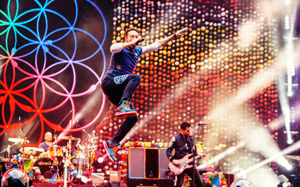 Coldplay Dreams Tour wallpaper Chris Martin mid-jump colorful lights geometric patterns vibrant stage