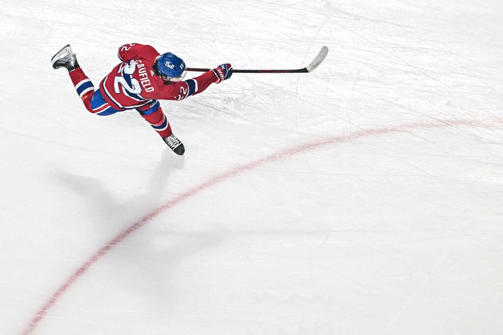 Cole Caufield mid-jump on ice in red jersey poised to strike puck dynamic hockey wallpaper background