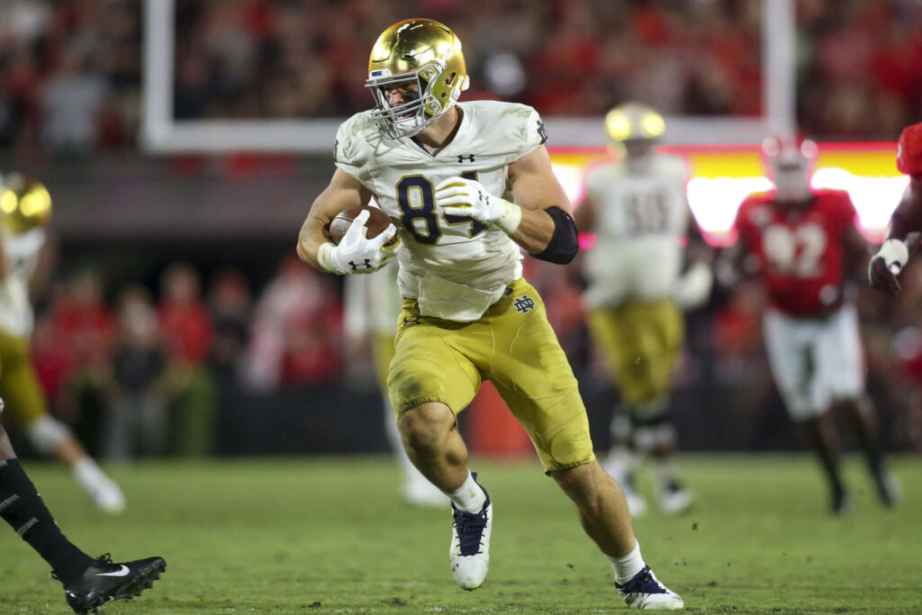 Cole Kmet Notre Dame football action running with gold helmet white jersey under stadium lights Wallpaper