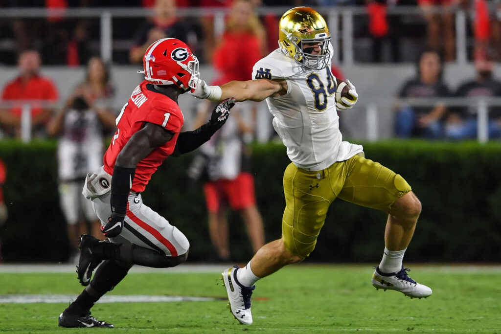 Cole Kmet stiff-arms Georgia defender running strong in Notre Dame football uniform action Wallpaper