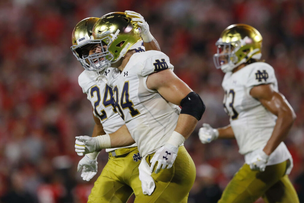 Cole Kmet Notre Dame football action shot in gold helmet white jersey blurred stadium background Wallpaper