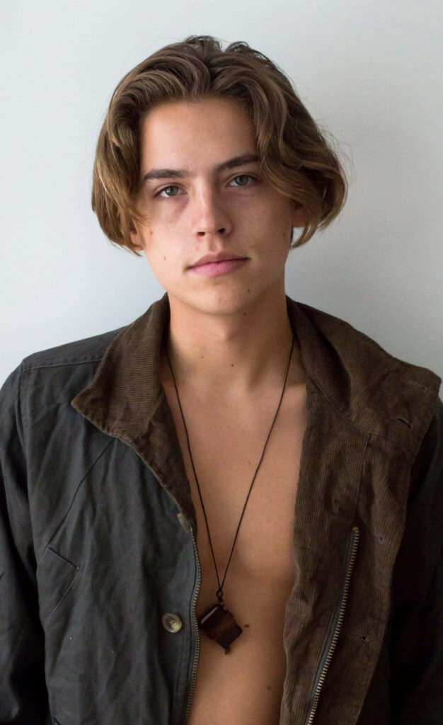 Cole Sprouse minimalist portrait in textured dark jacket with pendant necklace on white background Wallpaper