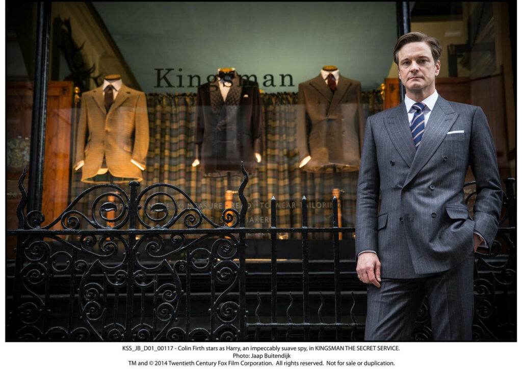 Colin Firth as Harry in sharp suit standing confidently by Kingsman tailor shop window wallpaper
