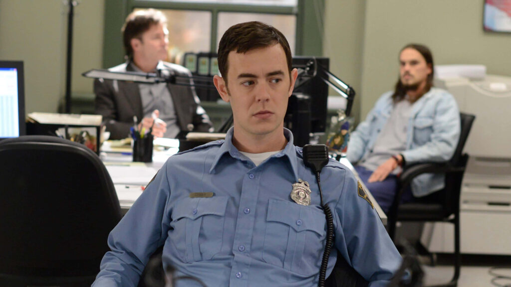 Colin Hanks as police officer in blue uniform in busy office with badge radio and colleagues Wallpaper