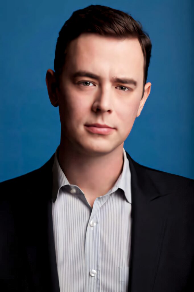 Colin Hanks professional portrait in dark suit jacket blue background cool toned wallpaper