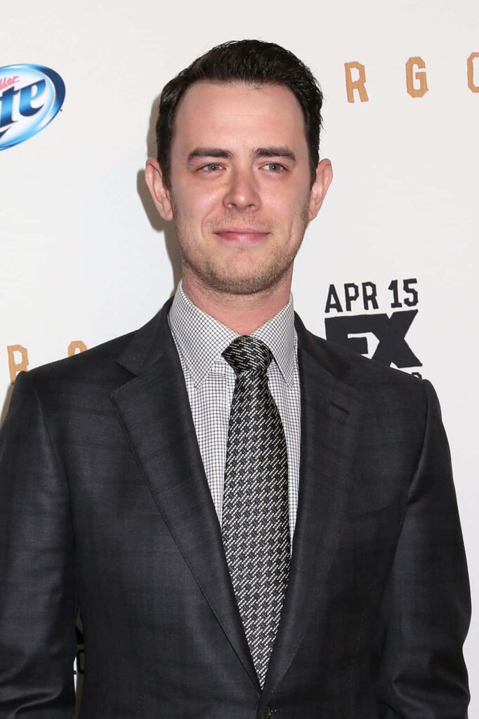 Colin Hanks in dark tailored suit and patterned tie on red carpet with bright event backdrop Wallpaper