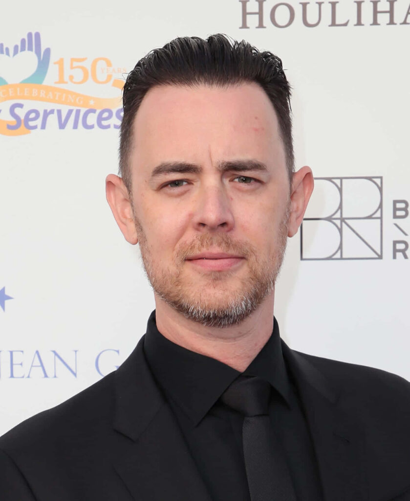 Colin Hanks in classic black suit and tie at event with bright backdrop confident celebrity portrait Wallpaper