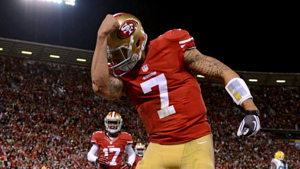 Colin Kaepernick celebrating in red gold 49ers jersey with vibrant stadium crowd background Wallpaper