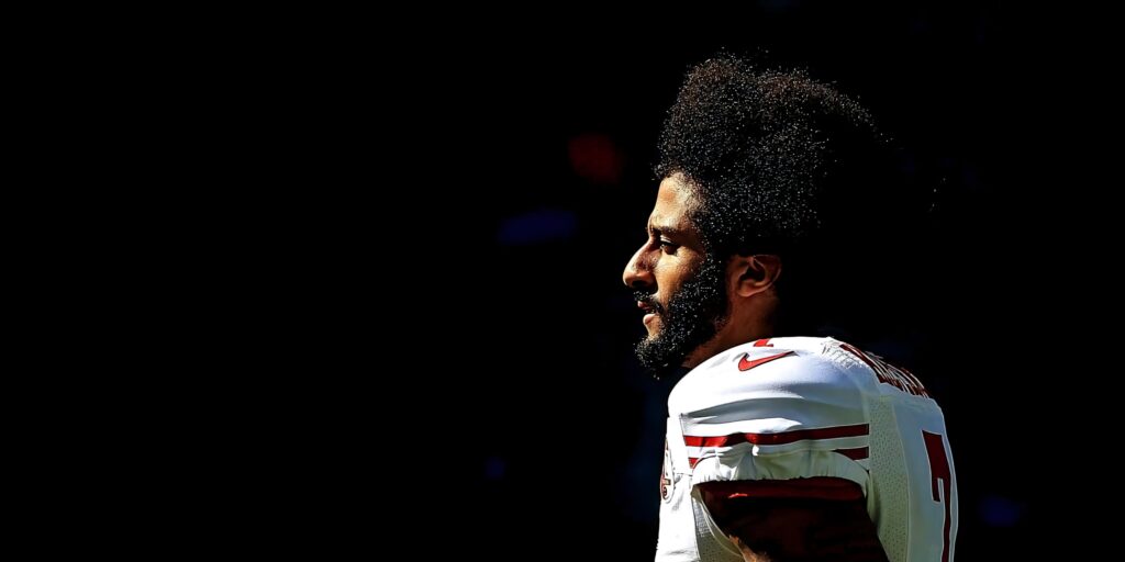 Colin Kaepernick in 49ers jersey profile with afro and focused expression on black background wallpaper