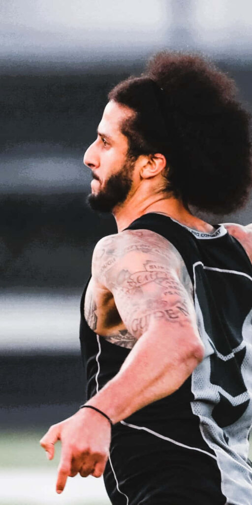 Colin Kaepernick in dynamic athletic pose with tattoos and signature hairstyle wallpaper background