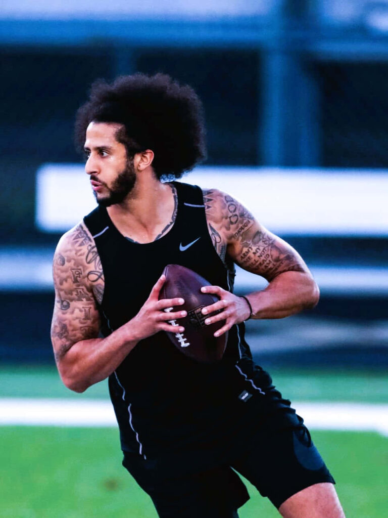Colin Kaepernick in black tank top and shorts showing tattoos and afro on football field background Wallpaper