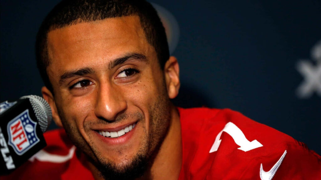 Colin Kaepernick in red jersey smiling at press conference vibrant NFL quarterback wallpaper background