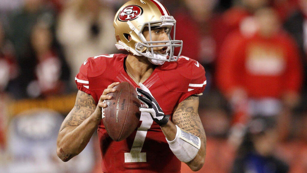 Colin Kaepernick in red and gold 49ers uniform focused during dynamic NFL game action wallpaper