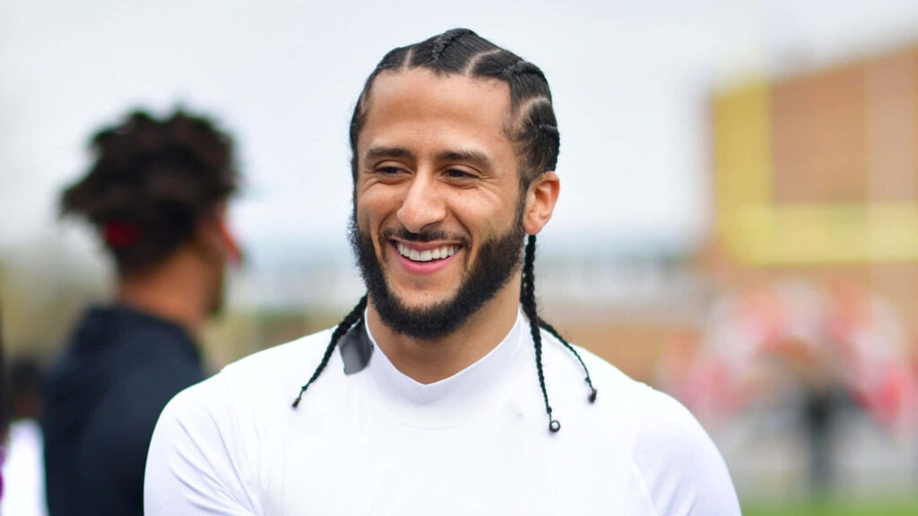 Colin Kaepernick smiling outdoors in white shirt with braided hair natural vibrant wallpaper background