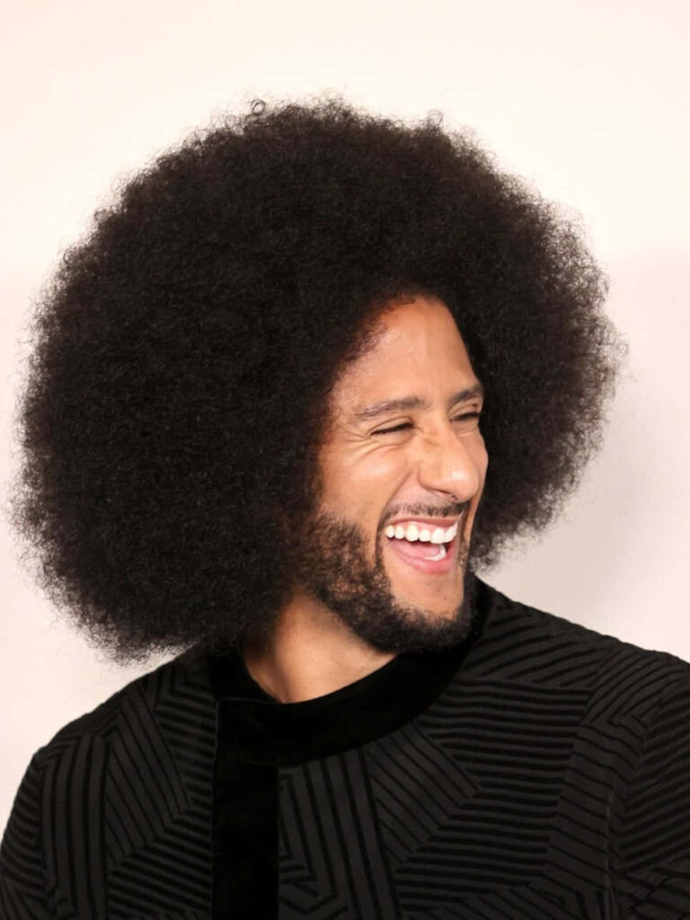 Colin Kaepernick close-up portrait smiling with iconic afro beard and modern geometric shirt background Wallpaper