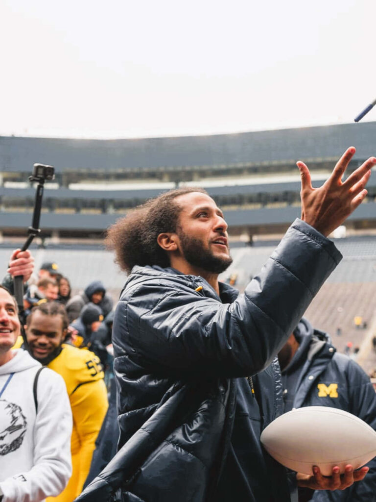 Colin Kaepernick tossing a football at stadium engaging fans vibrant sports spirit wallpaper background