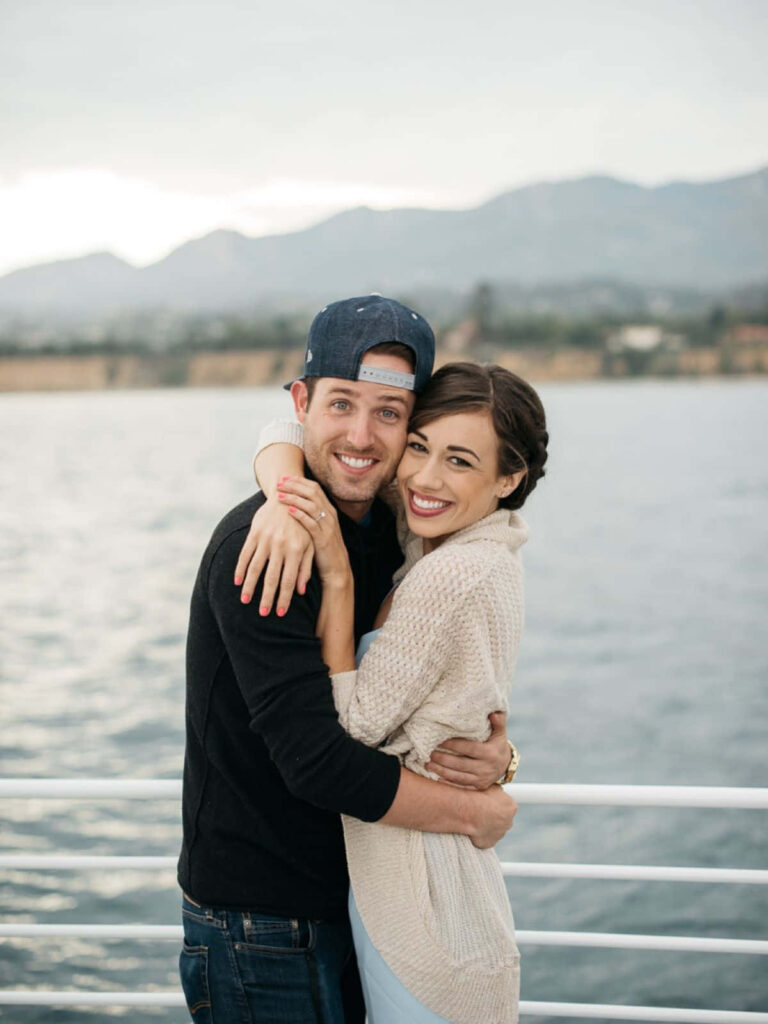 Colleen Ballinger and Joshua Evans embracing on boat with misty mountains sunset cruise background Wallpaper
