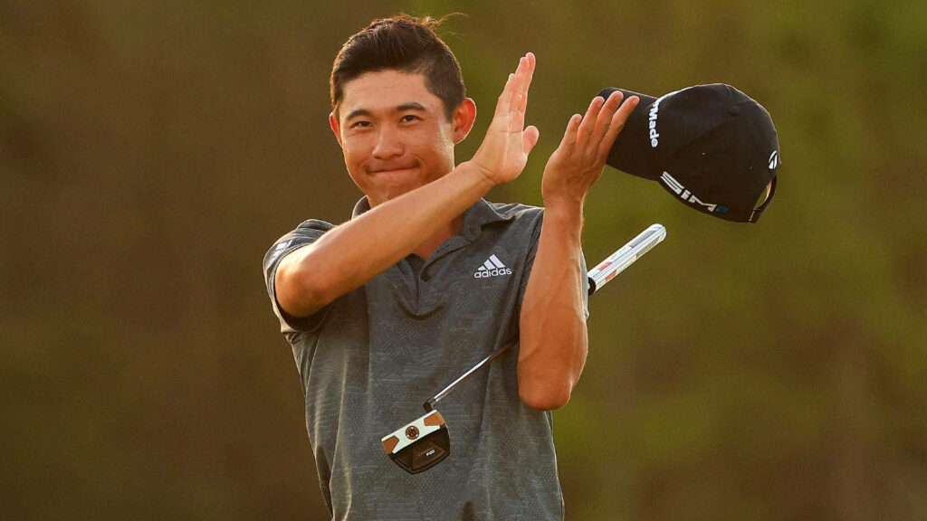 Collin Morikawa clapping with golf cap and putter in warm light sports wallpaper background