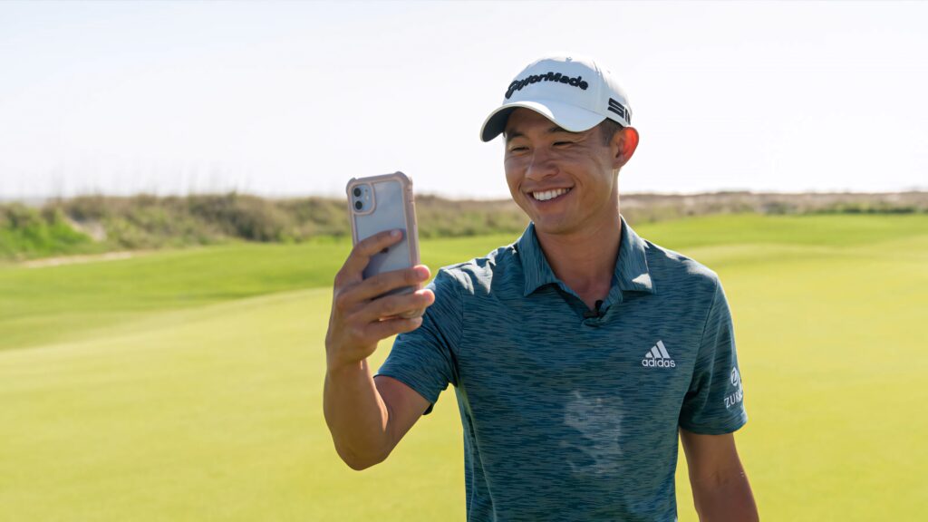 Collin Morikawa smiling on sunlit golf course wearing teal Adidas shirt and white TaylorMade cap Wallpaper