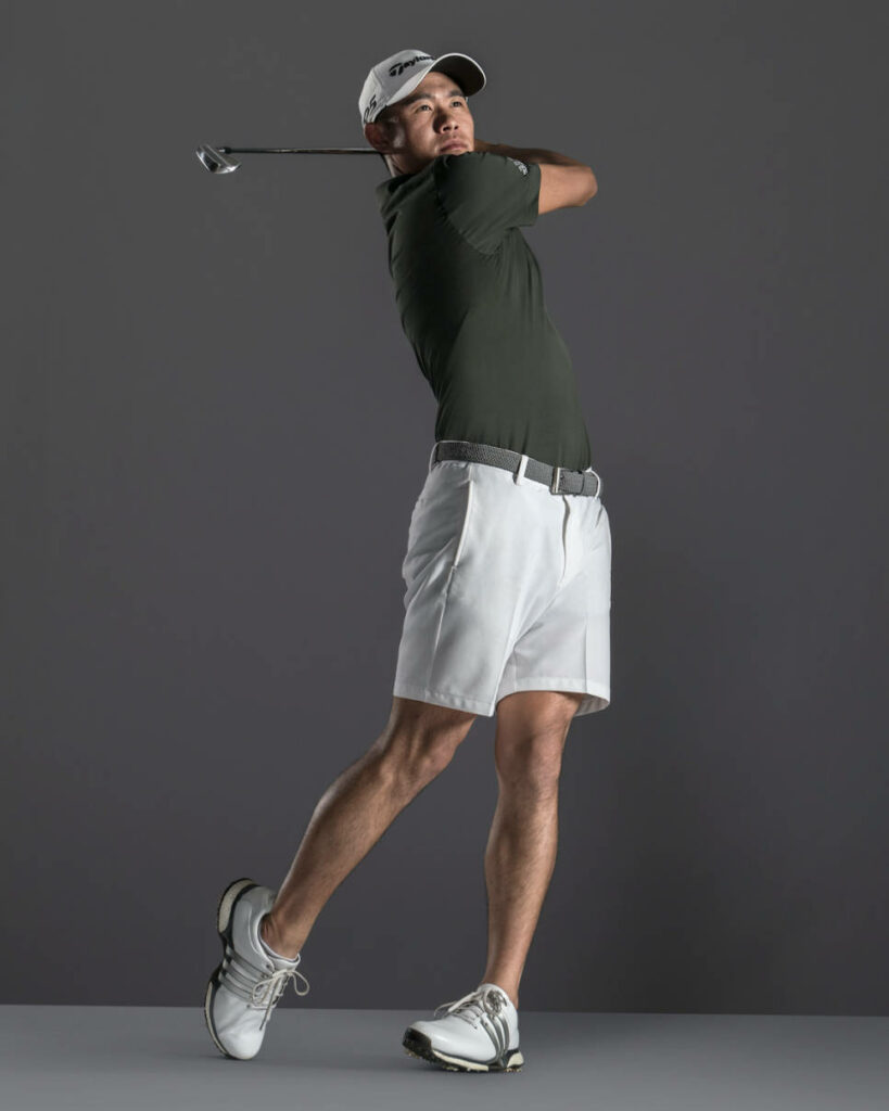 Collin Morikawa mid golf swing in studio wearing dark polo white shorts athletic focus wallpaper