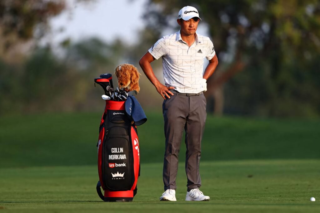 Collin Morikawa in stylish golf attire stands on green course with personalized golf bag before play Wallpaper