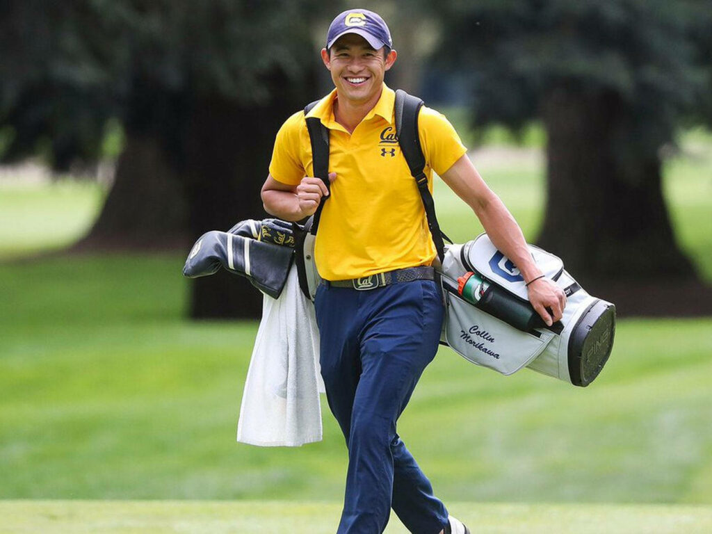 Collin Morikawa smiling on green golf course carrying clubs in yellow Cal polo and navy pants Wallpaper