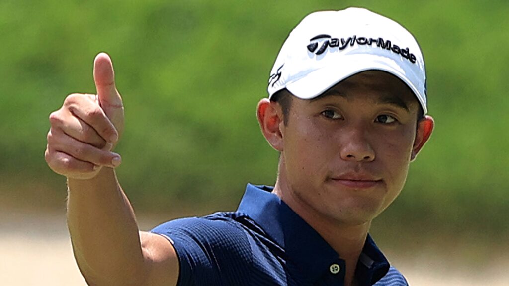Collin Morikawa thumbs up in navy polo and TaylorMade cap with blurred green golf background Wallpaper