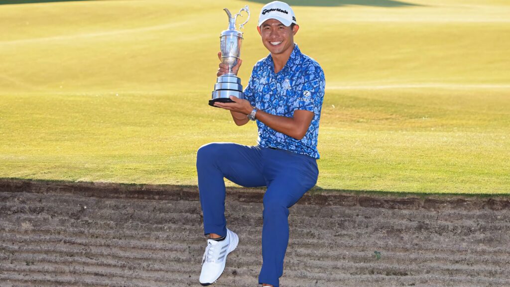 Collin Morikawa holding silver trophy sitting on grass in blue polo blue pants golf victory wallpaper