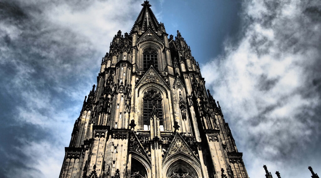 Gothic spires of Cologne Cathedral under moody sky showcasing intricate stonework wallpaper background