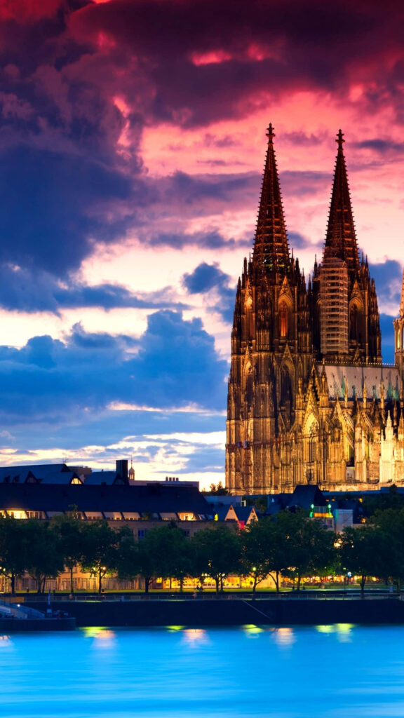 Cologne Cathedral Gothic architecture illuminated at sunset with colorful sky and water reflection Wallpaper