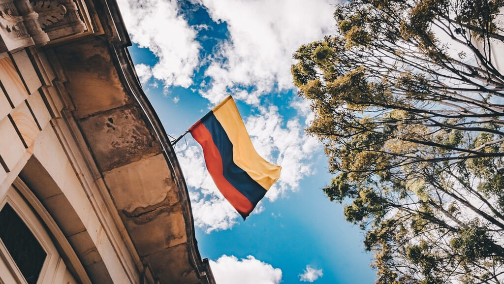 Colombian flag waving bright blue sky historic building lush green trees patriotic wallpaper