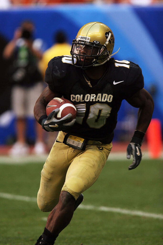 Colorado Buffaloes football player in black and gold uniform charges down sunlit field in action Wallpaper
