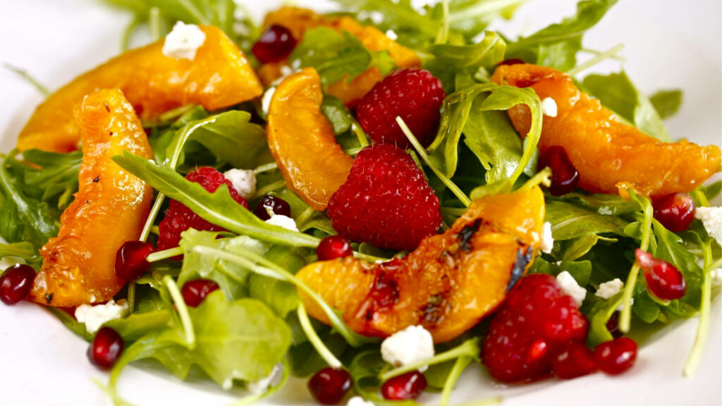 Colorful arugula salad with juicy peaches raspberries pomegranate seeds and crumbled cheese Wallpaper
